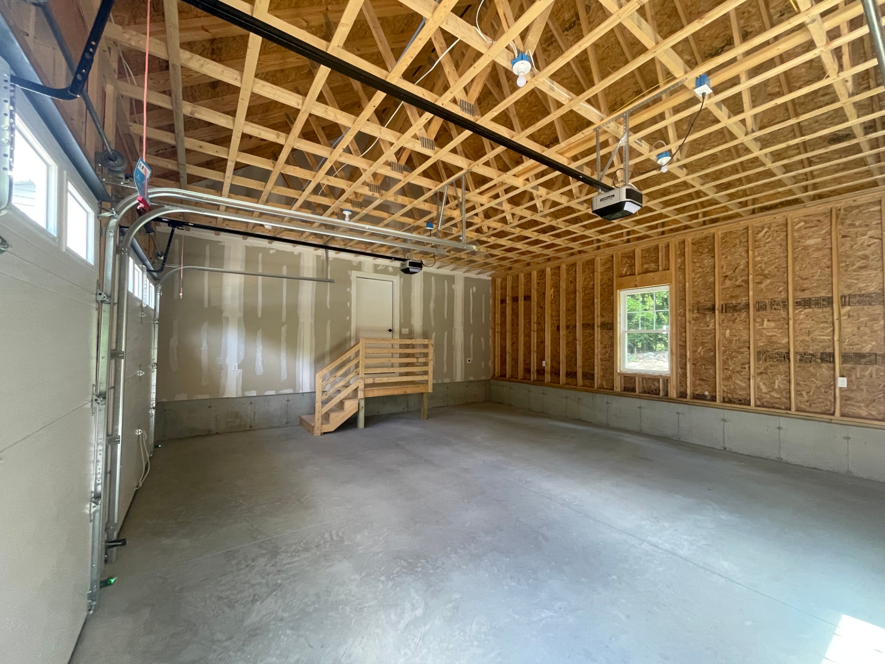 Two-car attached garage interior with exposed truss ceiling and openers installed