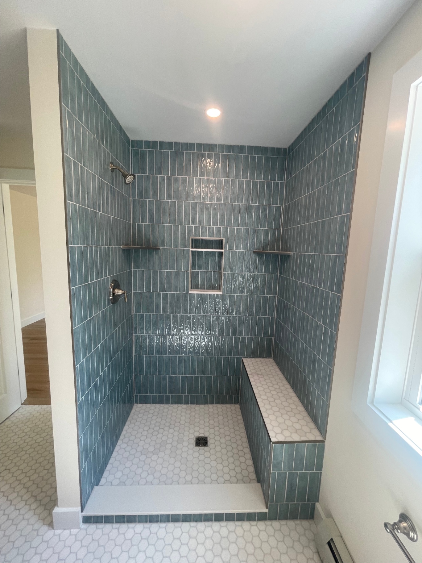 Custom walk-in tile shower with teal vertical subway tile, built-in bench, and hex mosaic floor