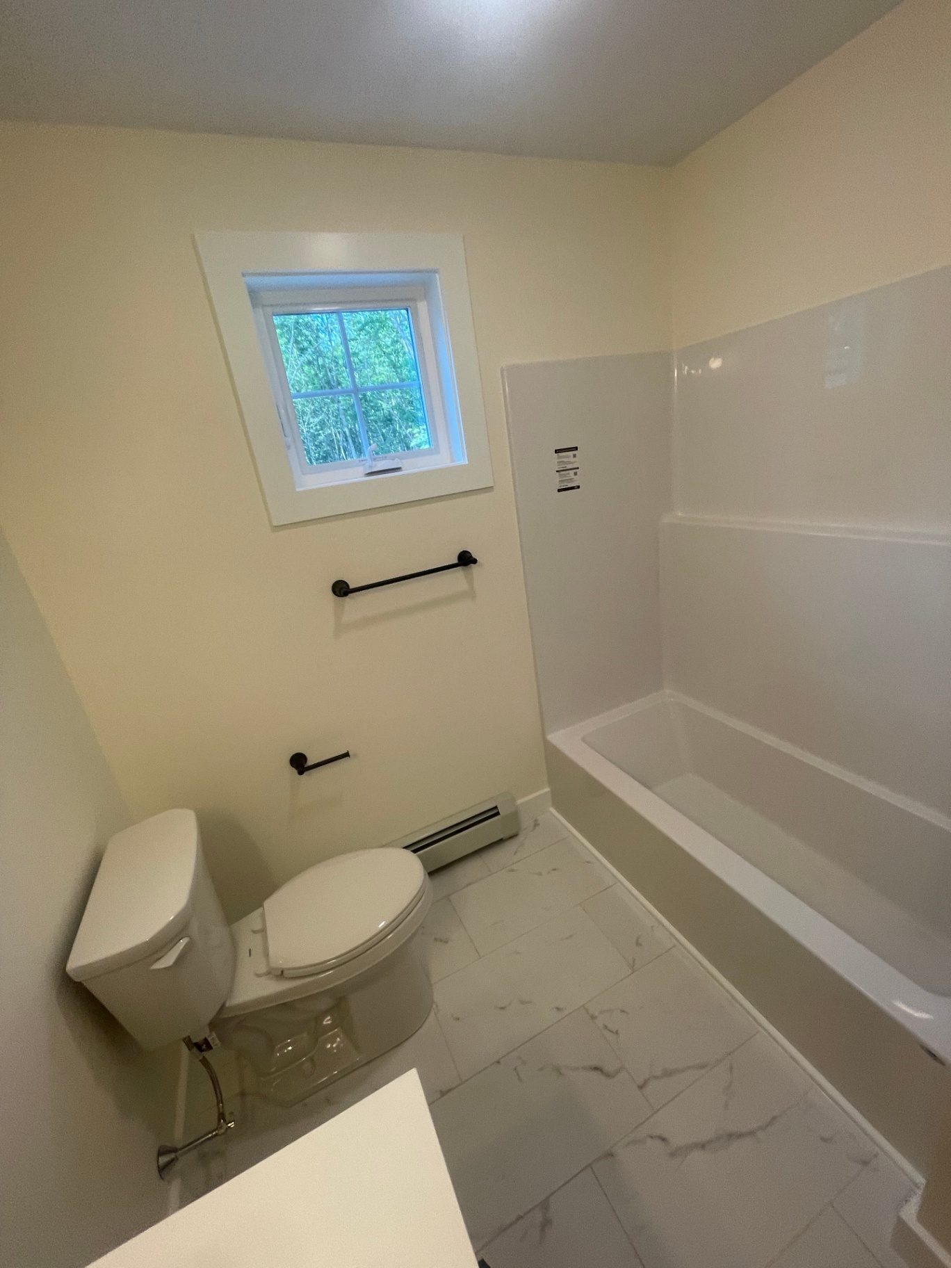 Guest bathroom with tub-shower combo, marble-look tile floor, and matte black fixtures