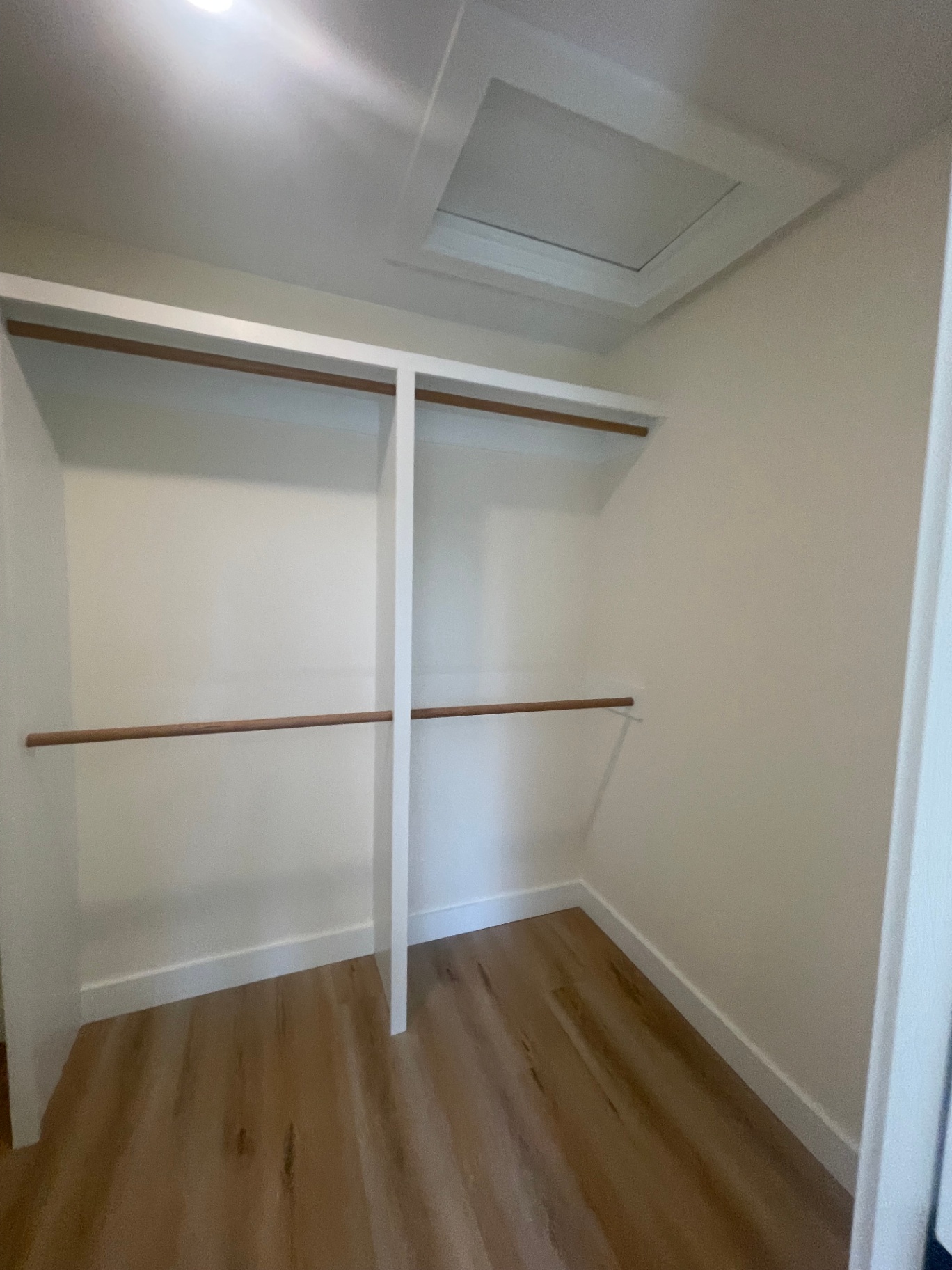 Walk-in closet with white built-in shelving, hanging rods, and attic access