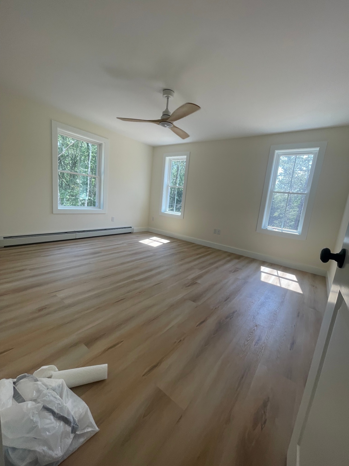 Sunlit bedroom with three windows, LVP flooring, and ceiling fan