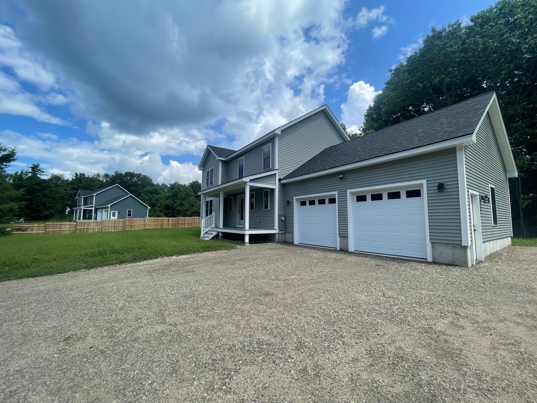 Finished sage-green two-story spec home with covered front porch and two-car garage in Springvale, Maine